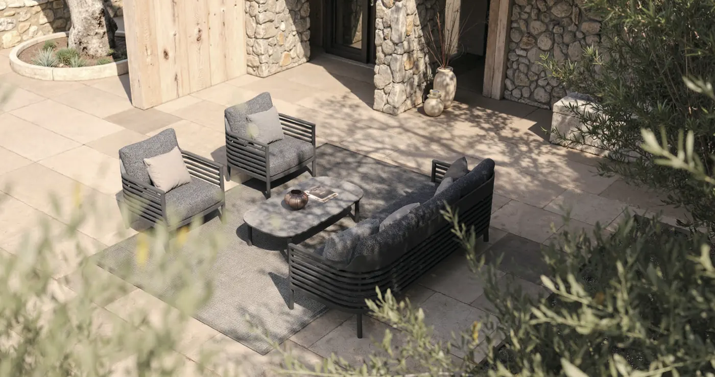 Factory rendering: New Perth lounge set in charcoal with a sofa, two lounge chairs and a coffee table on a sunlit stone patio