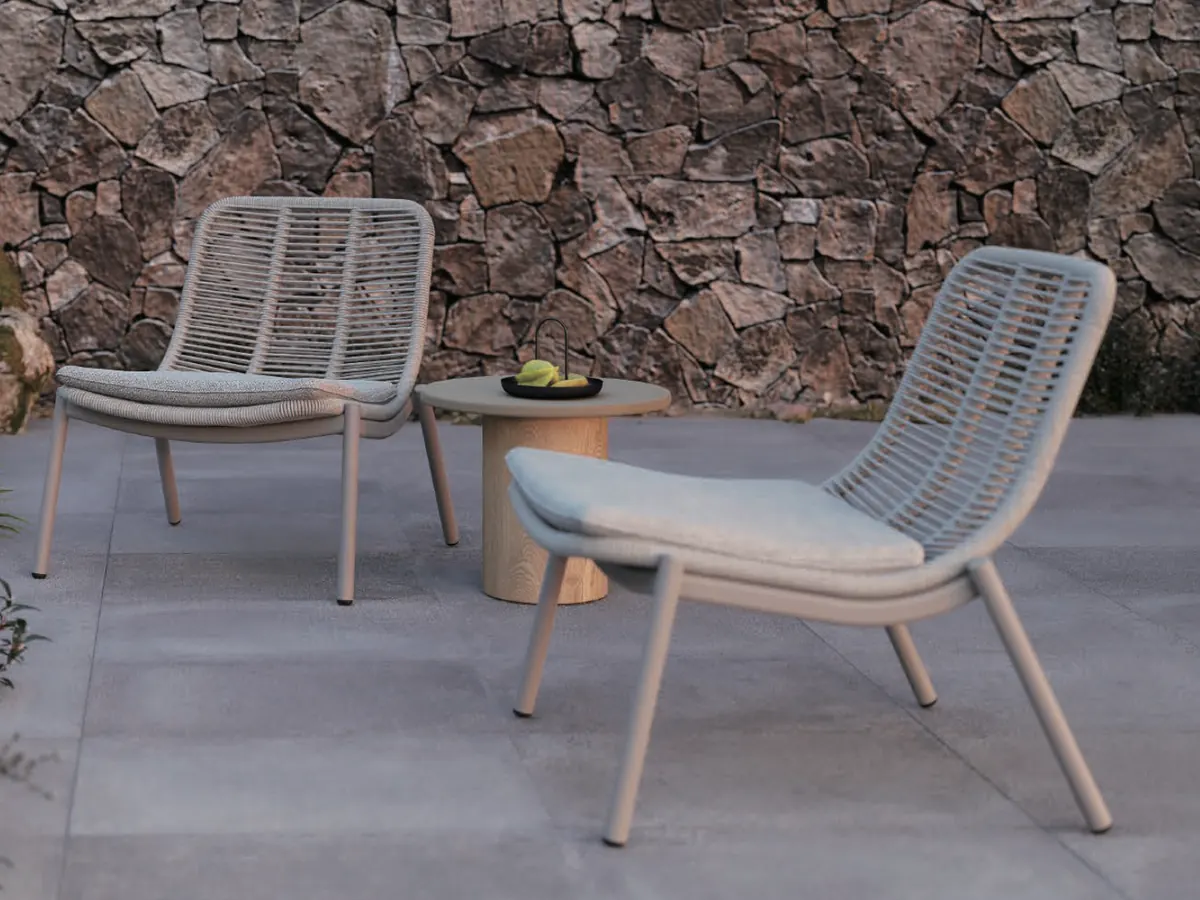 Two rope-back lounge chairs and a round side table on a stone terrace, shown in black and white